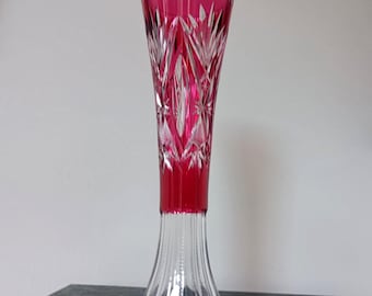 May include: A tall, slender vase featuring a deep magenta-colored upper section with intricate diamond and star-shaped cut glass patterns. The base is made of clear, colorless glass with vertical fluted ridges and a scalloped bottom edge.