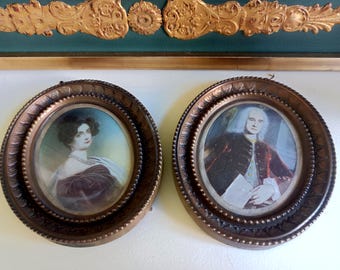May include: Two oval wall frames with ornate bronze-colored borders containing portrait prints. The left frame features a person with dark hair in a dark dress, while the right frame displays a person with white hair in a dark coat holding a paper.