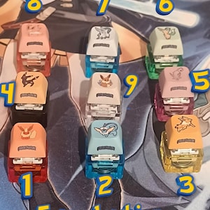 Könnte beinhalten: Eine Sammlung von neun farbenfrohen Tackergeräten, jedes mit einem anderen Pokémon-Charakter. Die Tacker sind in verschiedenen Farben erhältlich, darunter Rot, Blau, Grün und Gelb. Der Text "Eeveevolution Bundle" ist zu sehen.