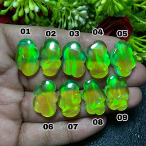 May include: Nine translucent, freeform gemstones with a mix of yellow and green hues are displayed. Each stone is numbered from 01 to 09. The gemstones are set against a blurred background of green foliage and a dark surface.