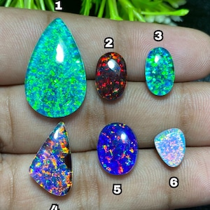 May include: A collection of six polished opal gemstones in various shapes. The opals display a range of colors, including green, blue, red, and purple, with iridescent patterns. The gemstones are teardrop, oval, and triangular shaped.