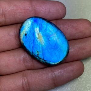 Puede incluir: Una piedra preciosa de labradorita ovalada de color azul y blanco con un brillo iridiscente.