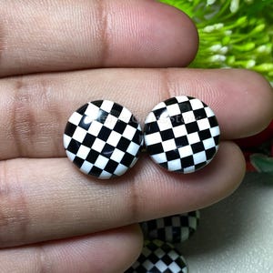 May include: A pair of black and white checkered round earrings. The earrings are made of a glossy material and have a checkerboard pattern.
