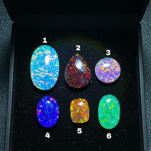 May include: A collection of six opals displayed in a black box. The opals vary in shape and color, including blue, red, orange, and green. Each opal has a unique pattern and internal fire, showcasing their natural beauty.