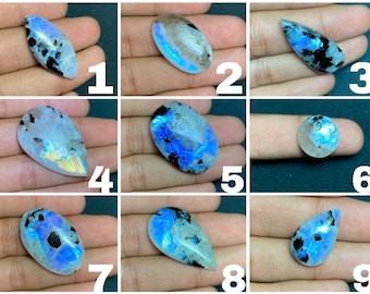 May include: Nine iridescent moonstone cabochons in various shapes and sizes, with a blue and white iridescent sheen. The stones are set in a hand, with the numbers 1 through 9 visible in the background.
