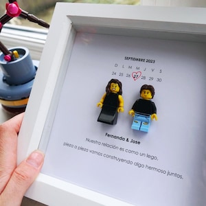 May include: A white framed artwork with two Lego figures representing a couple. The calendar shows September 2023, with the 27th circled in red. Text reads "Fernanda & Jose" and a Spanish quote about building a relationship.