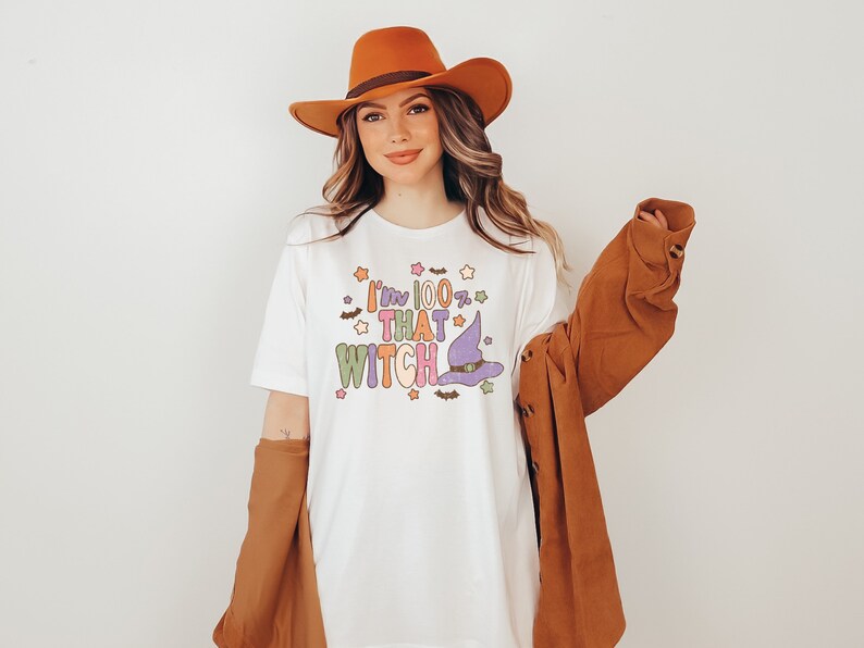 May include: White t-shirt with a colorful graphic that says "I'm 100% That Witch" with a witch's hat and stars.