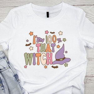 May include: White t-shirt with a graphic design that says "I'm 100% That Witch" in colorful letters with a purple witch hat and stars.