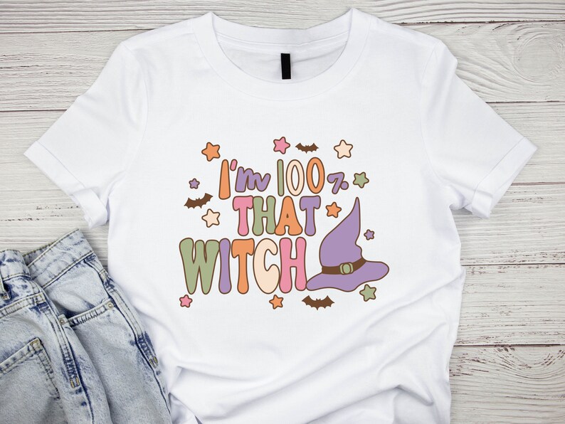 May include: White t-shirt with a graphic design that says "I'm 100% That Witch" in colorful letters with a purple witch hat and stars.
