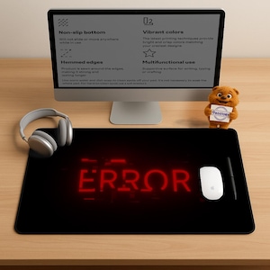 Puede incluir: Alfombrilla de ratón rectangular negra con la palabra "ERROR" en letras rojas de neón. Un ratón blanco, un bolígrafo negro y unos auriculares plateados están sobre la alfombrilla. Un monitor de ordenador y un pequeño oso de peluche están en el fondo.