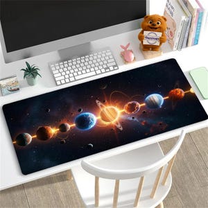 Pode incluir: Um tapete de mesa longo e retangular com uma representação vibrante de planetas em uma galáxia. O design inclui planetas com anéis, orbes brilhantes e um esquema de cores azul escuro e laranja. O tapete está em uma mesa branca.