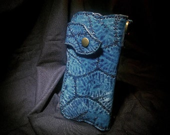 May include: A blue leather wallet with a textured, stitched pattern. The wallet has a flap with a brass button closure. The leather is dyed in shades of blue, creating a unique, handcrafted appearance.