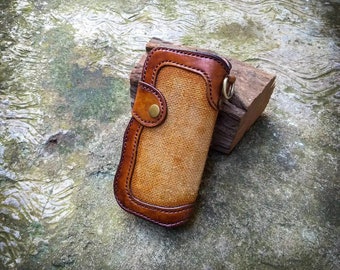 May include: A brown leather wallet with a tan canvas interior and a brass snap closure. The wallet has a stitched design and a metal loop for a key chain.