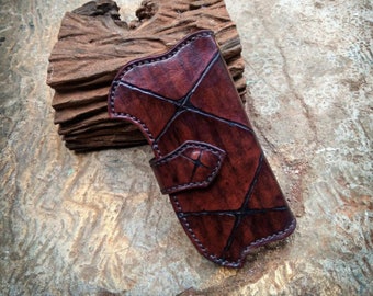 May include: A brown leather phone case with a geometric pattern. The case has a flap that closes with a snap.