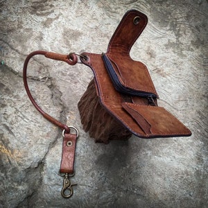 May include: A brown leather wallet with a long strap and a metal clasp. The wallet is open and has multiple compartments.