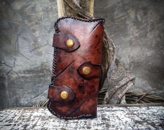 May include: A brown leather phone case with decorative stitching and three brass accents. The case has a distressed look and is designed to protect a phone.