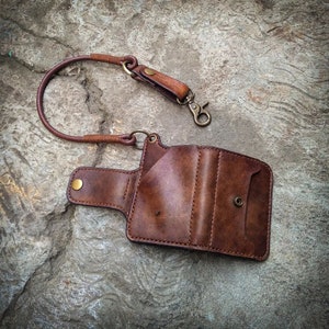 May include: A brown leather wallet with a chain attached. The wallet has multiple compartments and a snap closure. The chain is made of metal and has a clasp.