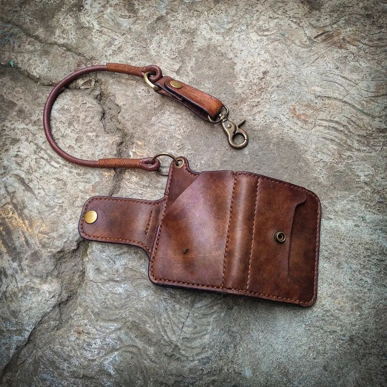 May include: A brown leather wallet with a chain attached. The wallet has multiple compartments and a snap closure. The chain is made of metal and has a clasp.