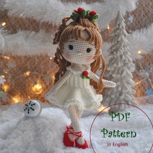 May include: A handmade crochet doll with long brown hair, wearing a white dress and red ballet shoes. The doll has a floral crown and a red rose. The image includes the text "PDF Pattern in English". The doll is standing on a snowy surface.