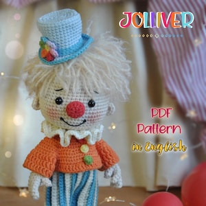 Peut inclure: Une poupée clown au crochet avec un chapeau haut de forme bleu clair orné d'une fleur arc-en-ciel. Le clown a un nez rouge, une chemise orange et un pantalon rayé bleu et blanc. Le texte "PDF Pattern in English" est visible.