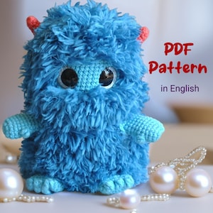 Puede incluir: Juguete de amigurumi de monstruo azul tejido a crochet con grandes ojos negros y cuernos rojos. Patrón PDF en inglés.