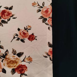 May include: A white fabric with a floral pattern of pink and orange roses. The fabric is next to a solid dark blue fabric.