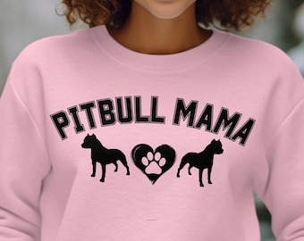 Puede incluir: Sudadera rosa con texto negro que dice "Pitbull Mama" y una silueta negra de un pitbull a cada lado de un corazón con una huella de pata dentro.
