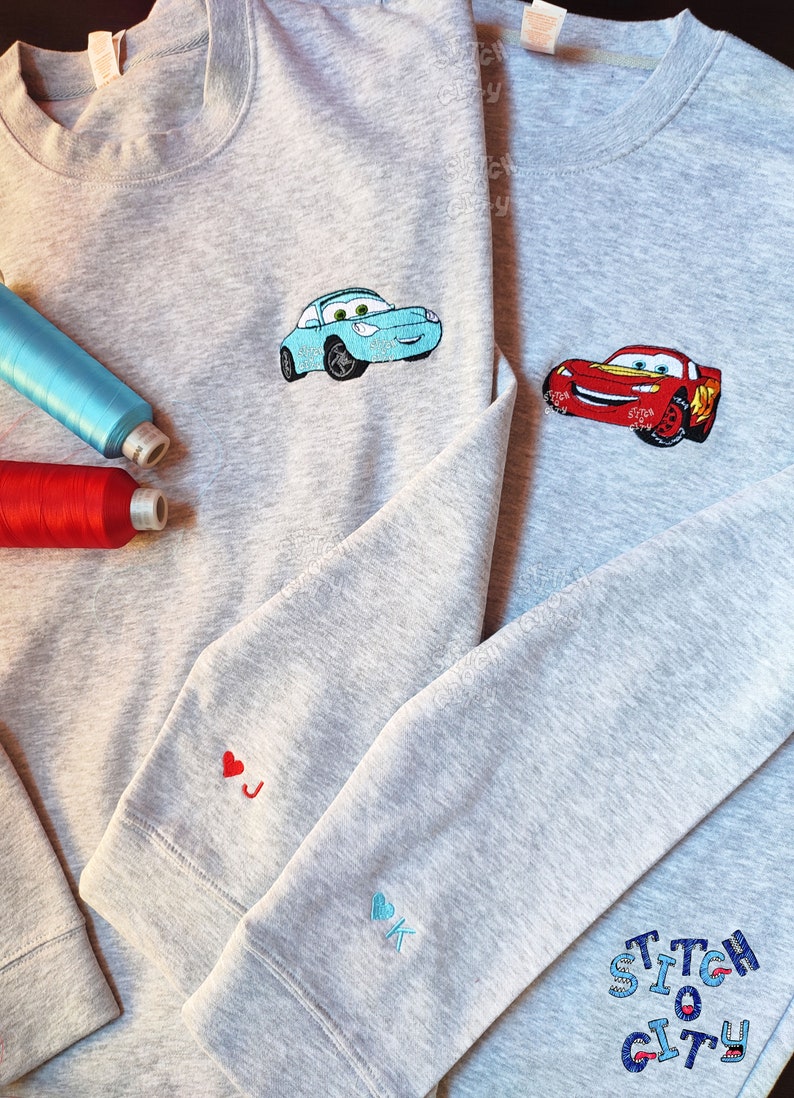May include: Two gray sweatshirts with embroidered Cars characters. One sweatshirt has a blue Lightning McQueen and the other has a red Mater. The sleeves have embroidered hearts with the initials J and K.
