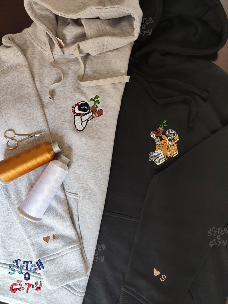 May include: Two hooded sweatshirts with embroidered designs. The gray sweatshirt has a robot holding a plant and the text "Stitch So City". The black sweatshirt has a robot holding a plant and the text "Stitch So City".