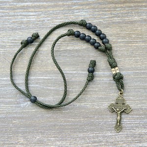 以下が含まれることがあります： 濃い緑色のコードと黒いビーズのロザリオ。ロザリオは、イエス・キリストの詳細な描写が施されたブロンズ色の十字架が特徴です。コードは結び目があり、小さな装飾的な十字架が付いています。