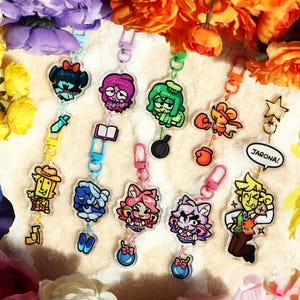 May include: A collection of eight acrylic character keychains featuring diverse cartoon figures, including a mouse with boxing gloves, a character with a pan, and one with a speech bubble saying JARONA!, all attached to colourful plastic clasps.