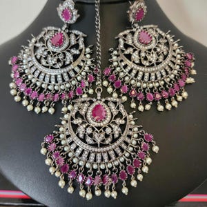 May include: A pair of silver earrings with pink stones and pearl accents. The earrings are connected by a chain.