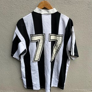 May include: A short-sleeved, collared jersey with black and white vertical stripes. The number "77" is prominently displayed on the back in a distressed, off-white font. The jersey has a white collar and sleeve stripes.