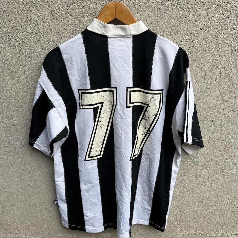 May include: A short-sleeved, collared jersey with black and white vertical stripes. The number "77" is prominently displayed on the back in a distressed, off-white font. The jersey has a white collar and sleeve stripes.