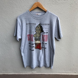 Pode incluir: Uma camiseta cinza com um gráfico de Astro Boy da série de mangá japonesa "Astro Boy" de Osamu Tezuka. O gráfico inclui o texto "Science Fiction" e detalhes sobre as características de Astro Boy. A camiseta tem uma etiqueta que diz "8714".