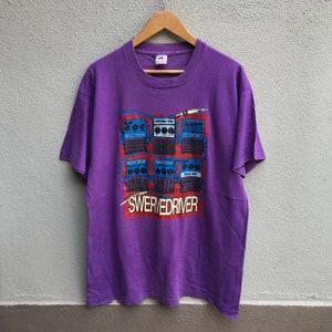 Könnte beinhalten: Lilafarbenes T-Shirt mit einem Aufdruck einer Band namens "Swerverdriver" und einer Reihe von Gitarrenpedalen mit Namen wie "Blue Down", "Deep Seat", "Overdrive", "Tufler 2", "Kayalist" und "Pick Up".