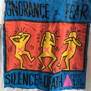 Pu&ograve; includere: Una maglietta bianca con una stampa grafica blu e rossa. La grafica presenta tre figure stilizzate gialle con le mani sulle orecchie. Il testo "IGNORANCE = FEAR" &egrave; stampato nella parte superiore della grafica e "SILENCE = DEATH" &egrave; stampato nella parte inferiore. Un triangolo rosa con il testo "FIGHT AIDS ACT UP" &egrave; stampato nell'angolo in basso a destra.