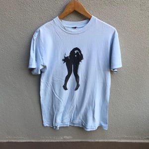 May include: A light blue t-shirt with a black and white graphic print of a woman's legs.