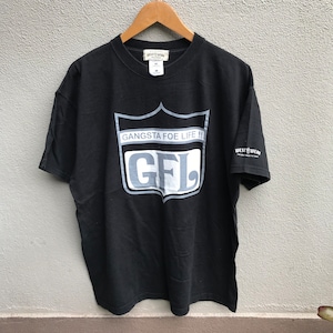 Puede incluir: Camiseta negra con un gráfico blanco de un escudo con el texto "Gangsta Foe Life!!" y "GFL" en su interior. La camiseta tiene una etiqueta blanca con el texto "Westwear" en la manga derecha.