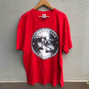 Puede incluir: Camiseta roja con un gráfico metálico plateado de un círculo con el texto "Full Surface Records" y un logotipo "FS" estilizado.