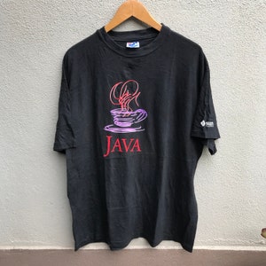Op de afbeelding: Zwart t-shirt met een kleurrijk ontwerp van een koffiekopje met stoom en het woord "JAVA" in het rood. Een klein "sun" logo staat op de mouw. Het t-shirt hangt aan een houten hanger.