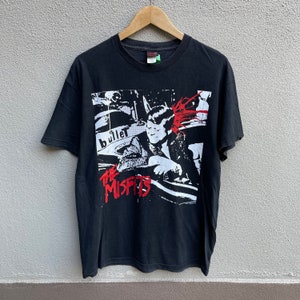 May include: Black t-shirt with a white and red graphic print of a band called "The Misfits". The graphic features a person in a car with the word "bullet" in the background.