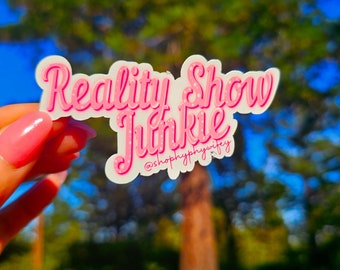 May include: Pink sticker with the text "Reality Show Junkie" and the social media handle "@shophypnotified".