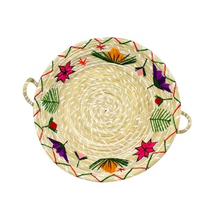 Op de afbeelding: Een ronde geweven dienblad met een decoratief geborduurd ontwerp met kleurrijke bloemen en bladeren. Het dienblad heeft twee handvatten aan de zijkanten.
