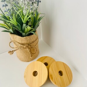 Puede incluir: Tres tapones redondos de botella de madera natural con un agujero en el centro. Los tapones est&aacute;n sobre una superficie blanca con un paquete de pajitas de vidrio transparentes.