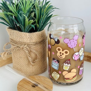 May include: A clear glass can with a straw and a bamboo lid. The can has a cartoon design featuring a mouse character, ice cream, and other Disney-themed imagery.