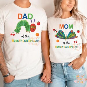 May include: Two white t-shirts with colorful graphics. One says "DAD" with a caterpillar design and the text "of the HUNGRY CATERPILLAR". The other says "MOM" with a butterfly design and the text "of the HUNGRY CATERPILLAR".