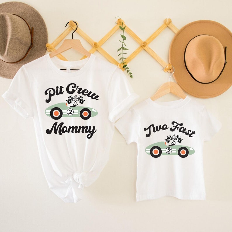 Pu&ograve; includere: Due magliette bianche con una grafica di un'auto da corsa verde. La maglietta pi&ugrave; grande dice "Pit Crew Mommy" e quella pi&ugrave; piccola dice "Two Fast".