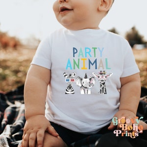Puede incluir: Un body blanco para beb&eacute; con el texto "PARTY ANIMAL" en azul, verde y amarillo. Tres animales de dibujos animados, una cebra, un elefante y una jirafa, llevan sombreros de fiesta y accesorios.