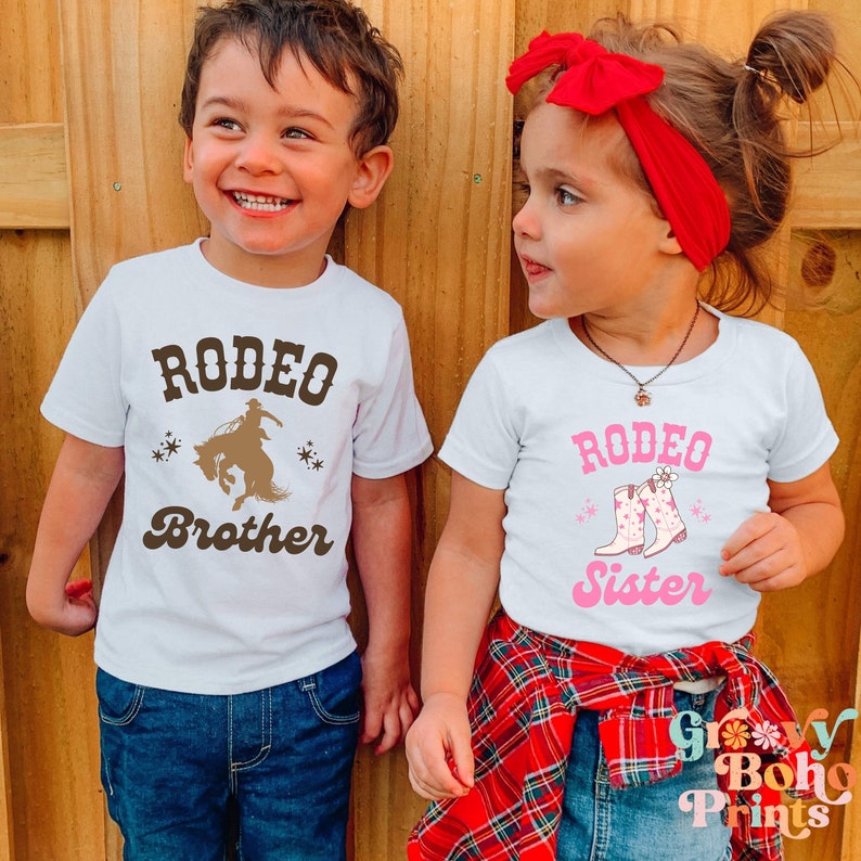 May include: Two children wearing white t-shirts with the text "Rodeo Brother" and "Rodeo Sister" printed on them. The boy is wearing blue jeans and the girl is wearing a red plaid skirt.